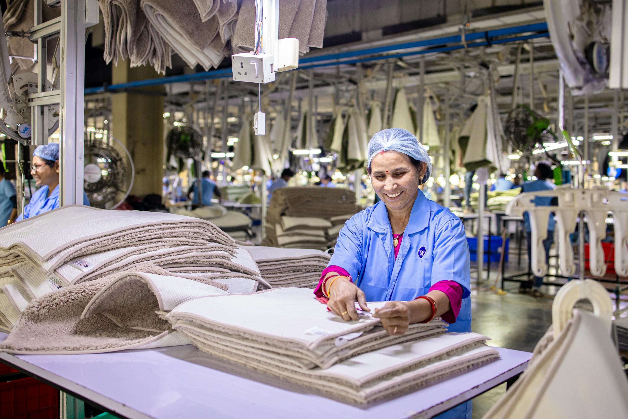 Cheerful textile worker folding fabric in a bright, busy factory environment.